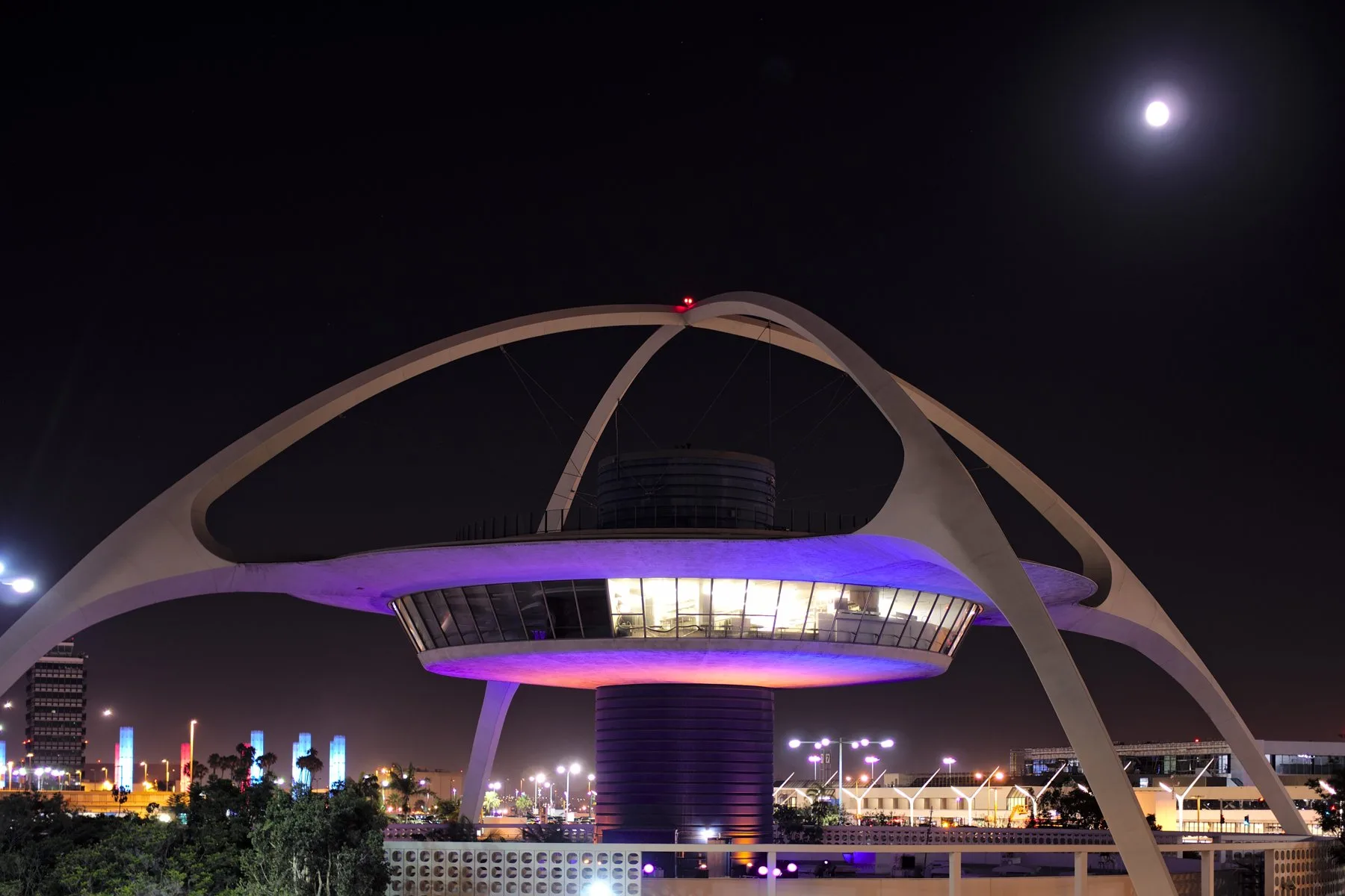 The LAX Theme Building lit up in purple at night in Los Angeles